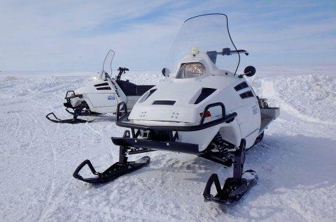 Two white snowmobiles parked on snow.